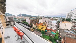 Una terraza en la azotea con sillas rojas, vistas de un paisaje urbano con diversos edificios y una montaña distante.