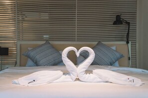 A hotel room with a bed, striped pillows, a heart-shaped towel arrangement, and a lamp. - Patong Penthouse 120m (Phuket)
