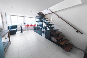 A modern kitchen with a unique spiral staircase, a dining area with red chairs, and a large window providing natural light. - Patong Penthouse 120m (Phuket)