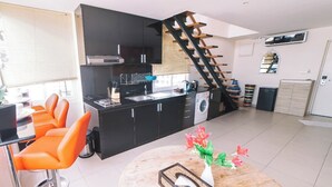 Una cocina moderna con armarios negros, lavadora integrada y una escalera de madera.