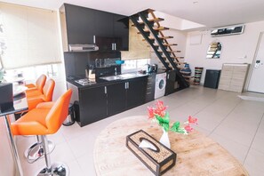 A modern kitchen with black cabinets, a built-in washing machine, and a wooden staircase. - Patong Penthouse 120m (Phuket)