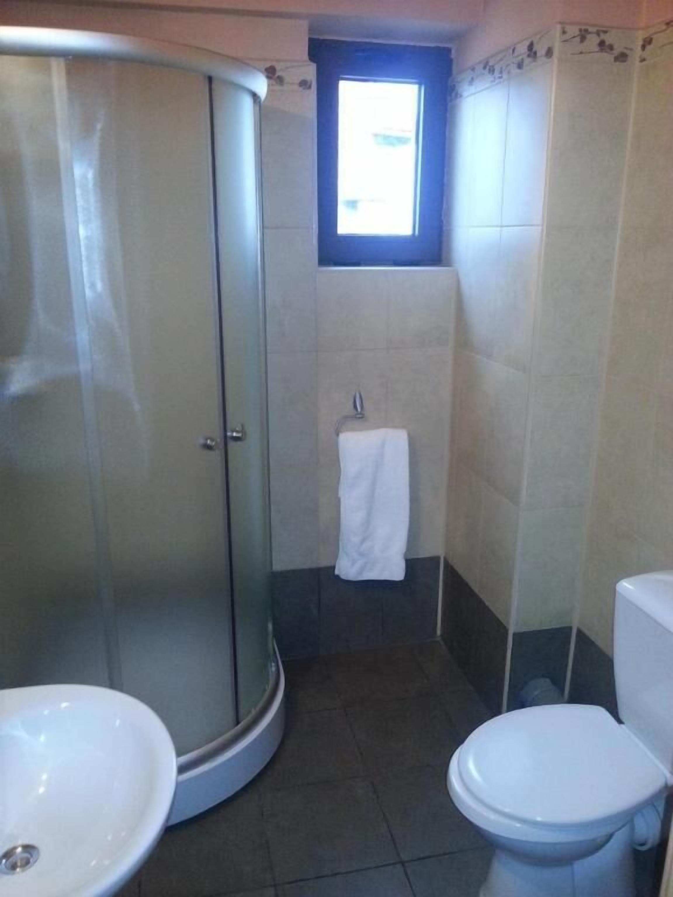Une salle de bain dotée d’une douche à parois de verre, d’un lavabo, de toilettes et d’une fenêtre laissant entrer la lumière naturelle.