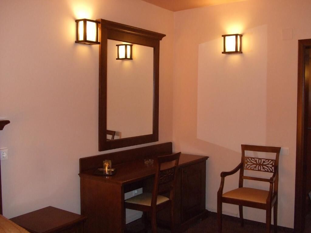 Une pièce comprenant un bureau en bois, une chaise, un grand miroir et deux lampes fixées au mur.