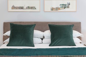 Uma cama com cabeceira marrom, duas almofadas verdes e um edredom branco.
