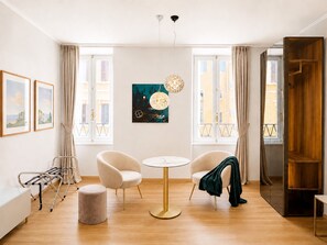 Een moderne hotelkamer met een ronde tafel, twee fauteuils, een bank, een hanglamp en een groot raam met gordijnen.