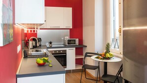 A compact kitchen with white cabinets, a microwave, a sink, and a small dining area with a table and chairs. - Design Apartment in Spanish Steps (Roma)