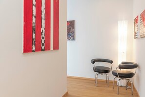 Une pièce avec un plancher en bois, deux chaises noires, une œuvre d’art aux couleurs rouge et blanche, et un petit tableau accroché au mur.