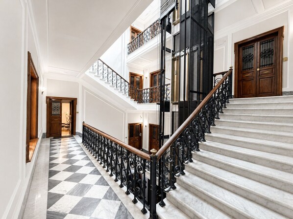 Een statige trap met marmeren treden en zwarte ijzeren balustrades die naar een vloer leidt.