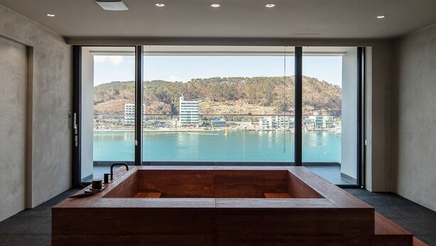 Une salle de bain moderne avec une grande baignoire, une vue sur un plan d’eau et un paysage urbain en arrière-plan.