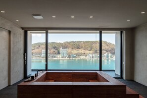 A modern bathroom with a large bathtub, a view of a body of water, and a cityscape in the background.