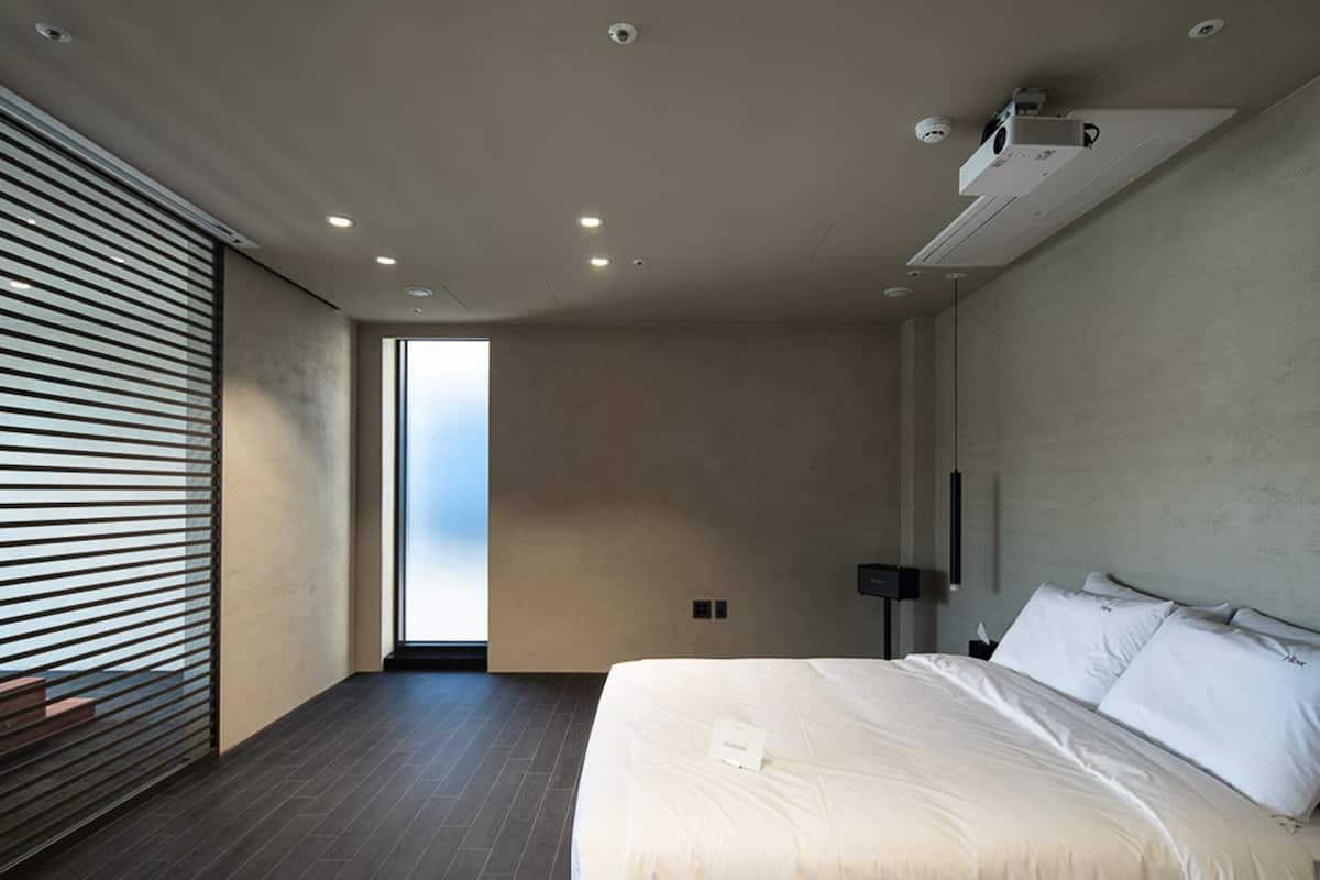 Quarto de hotel moderno com uma cama grande, vista pela janela e um projetor no teto.