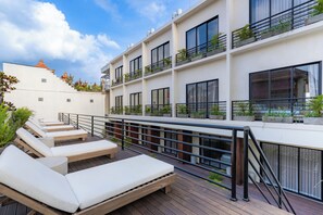 A rooftop terrace with sun loungers, a wooden deck, and a white building with balconies.