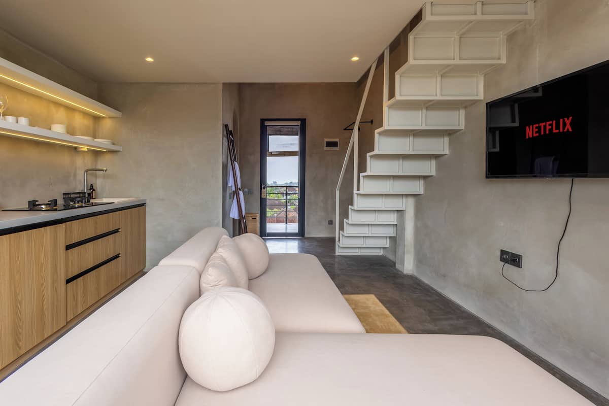 A modern kitchen with a built-in oven, a dining area with a white sofa, and a staircase leading to a balcony.