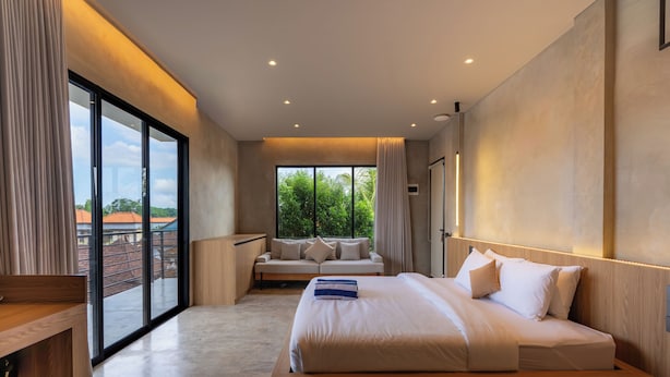 A modern bedroom with a large bed, a seating area, and a view through a sliding door. - Ubud Center Oasis by Betterplace (Ubud)