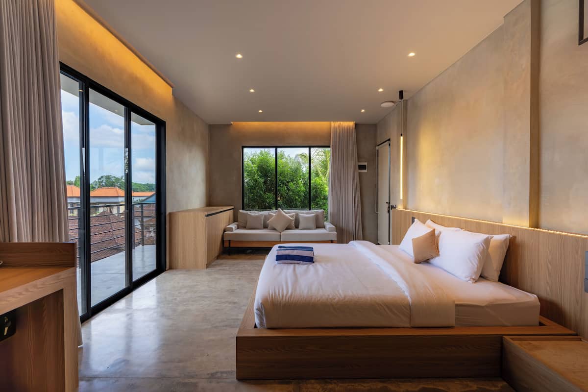 A modern bedroom with a large bed, a seating area, and a view through a sliding door.