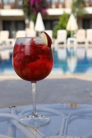 A glass of red drink with a garnish on a table by a pool. - HOTEL BİNLİK (Dalyan)