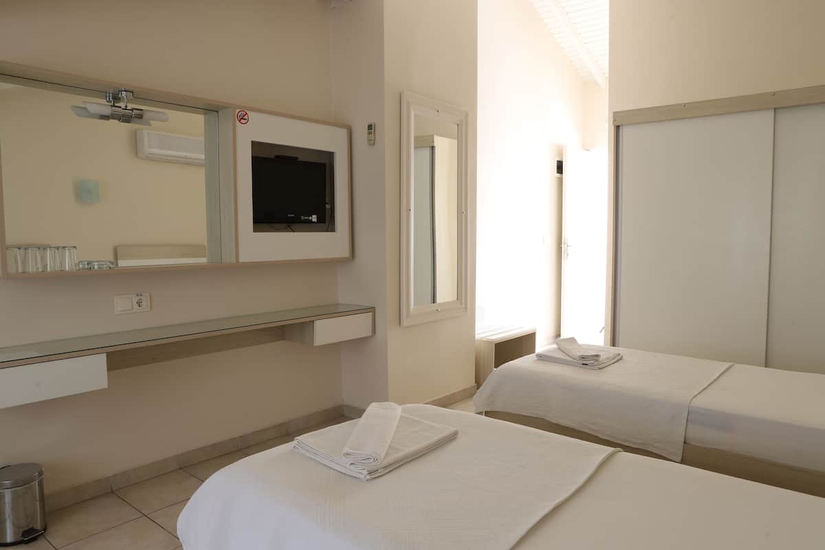 A hotel room with a bed, a bedside table, a mirror, a window, and a wall-mounted air conditioner.