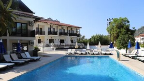 A swimming pool with lounge chairs and umbrellas, a building with balconies, and a clear sky. - HOTEL BİNLİK (Dalyan)