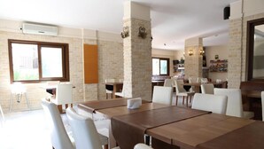 A spacious dining area with a long wooden table and white chairs, brick walls, and a large window. - HOTEL BİNLİK (Dalyan)