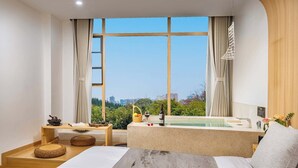 Ein modernes Hotelzimmer mit großem Fenster, einer Badewanne, einem Holztisch und einem Bett.