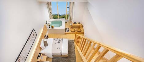 Een moderne hotelkamer met een houten trap, een groot raam met uitzicht op de stad, een jacuzzi en een klein balkon.