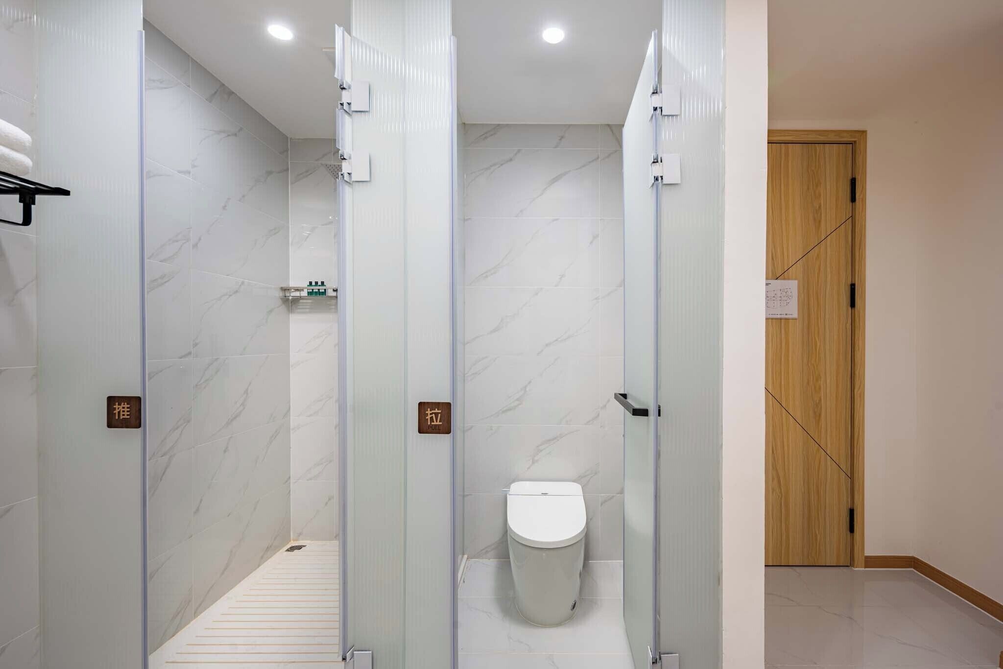 A modern bathroom with glass-enclosed shower stalls, a toilet, and a wooden door.