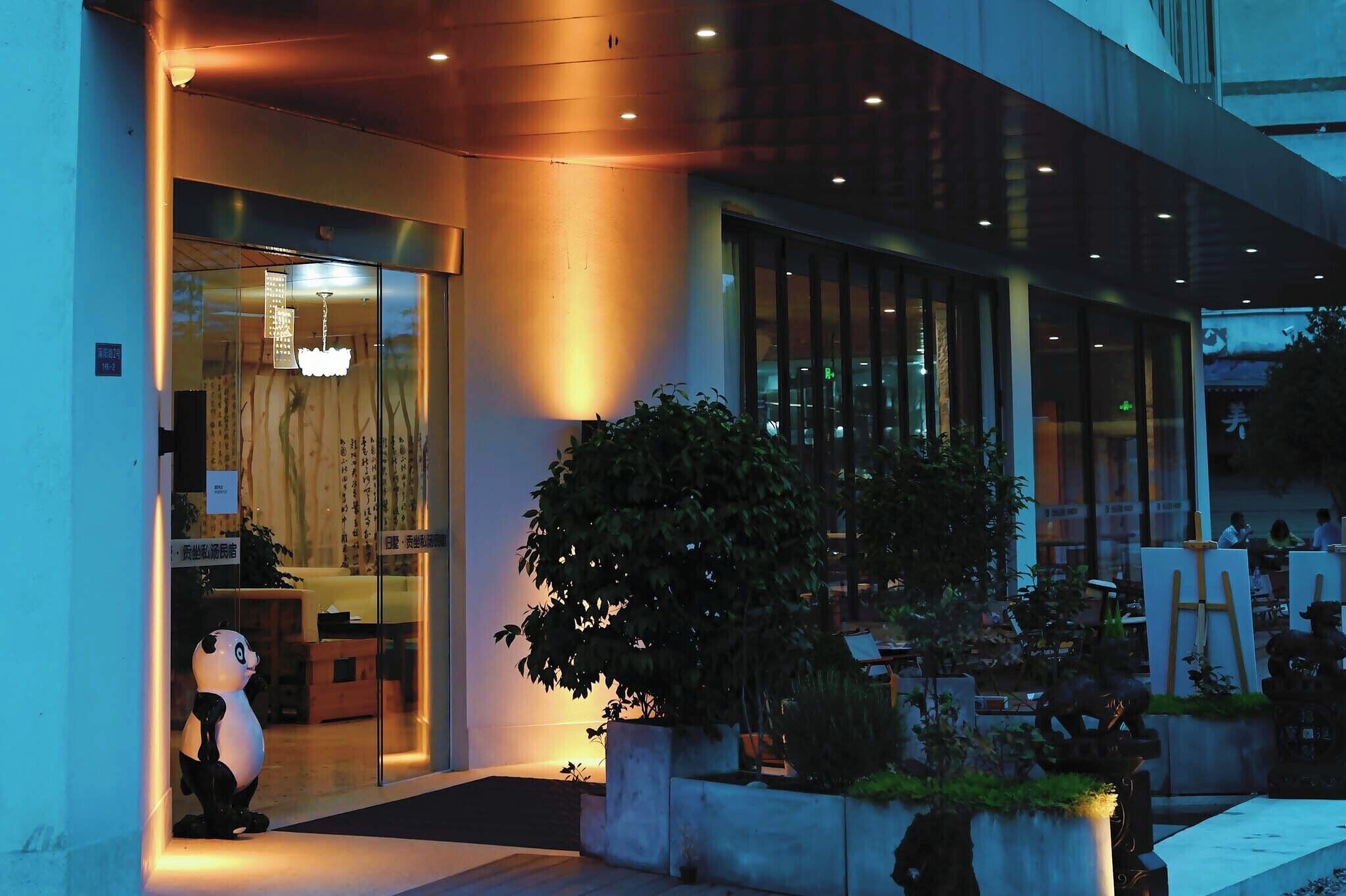 A modern building entrance with glass doors, a large indoor plant, and a panda statue.