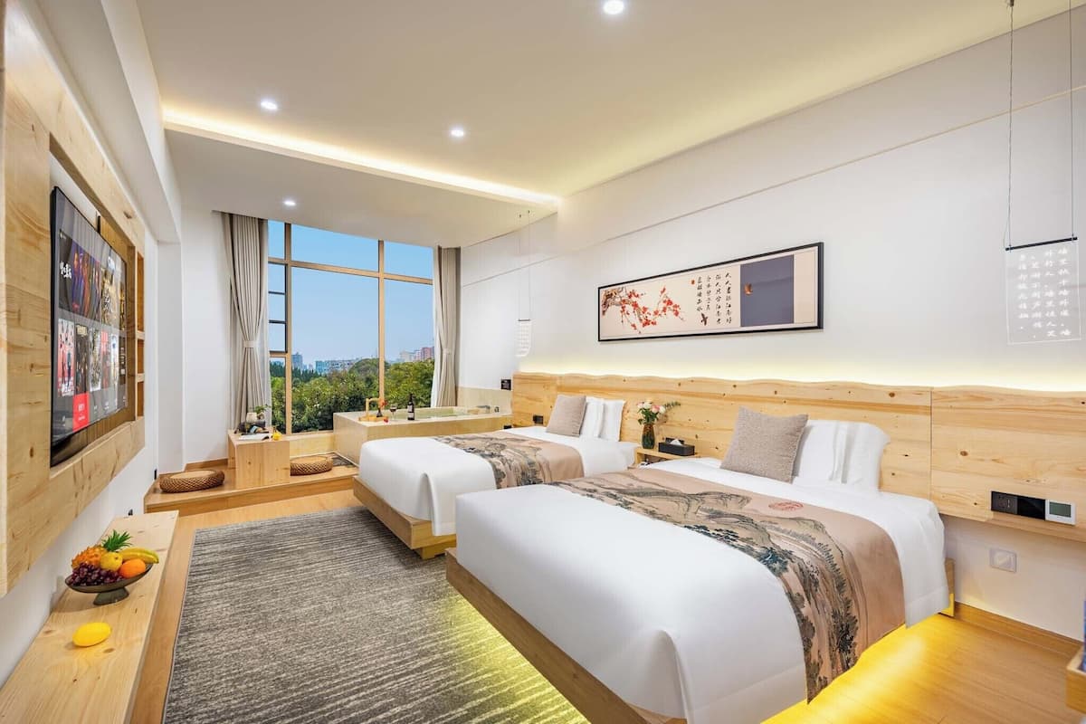 Habitación de hotel con dos camas, un ventanal grande, cabecero de madera y televisor montado en la pared.