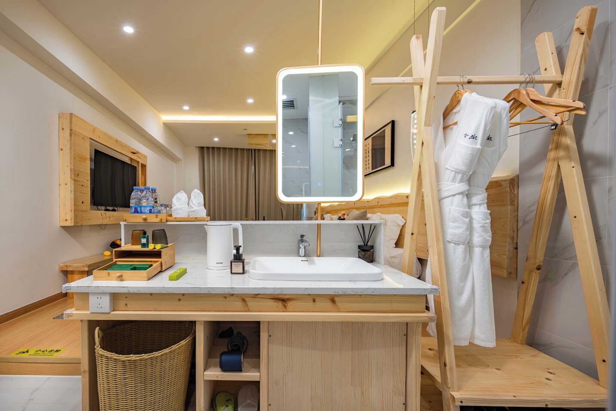A modern bathroom with a wooden vanity, a large mirror, and a wooden drying rack.