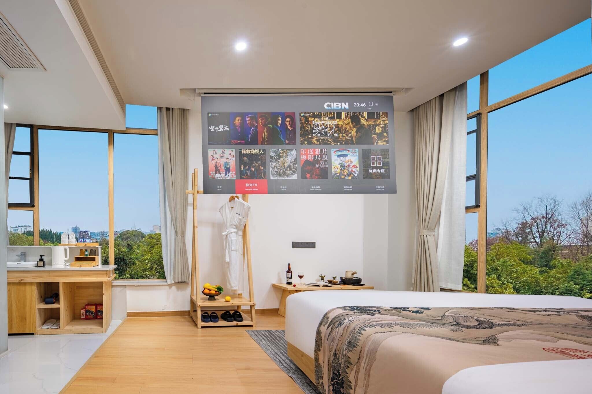 Habitación de hotel moderna con una cama grande, un televisor montado en la pared, un escritorio pequeño con un hervidor de agua y vistas al exterior.