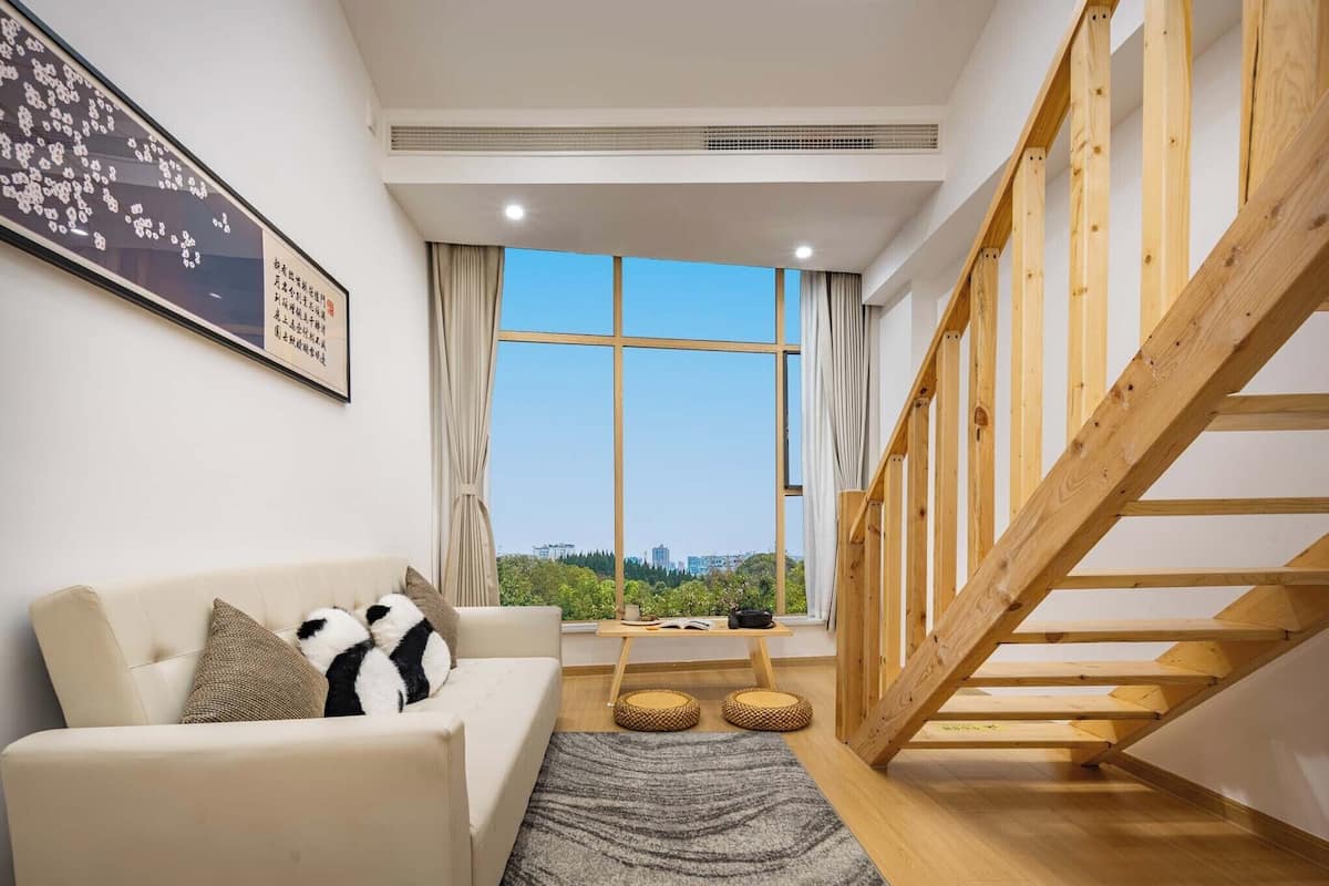 Una sala de estar moderna con un sofá, una escalera de madera y un ventanal con vistas a la ciudad.