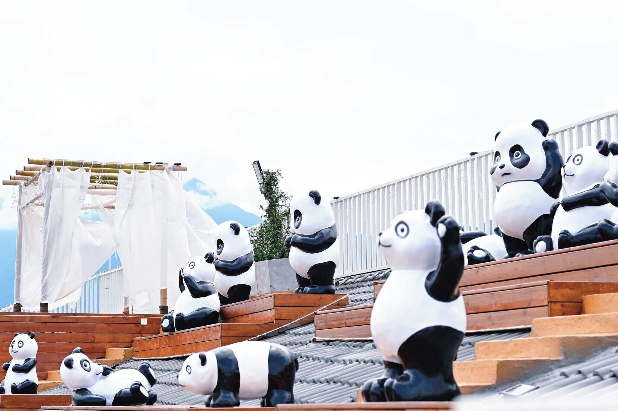 Grans estàtues de panda en una terrassa amb una escala de fusta i una tanca blanca al fons.