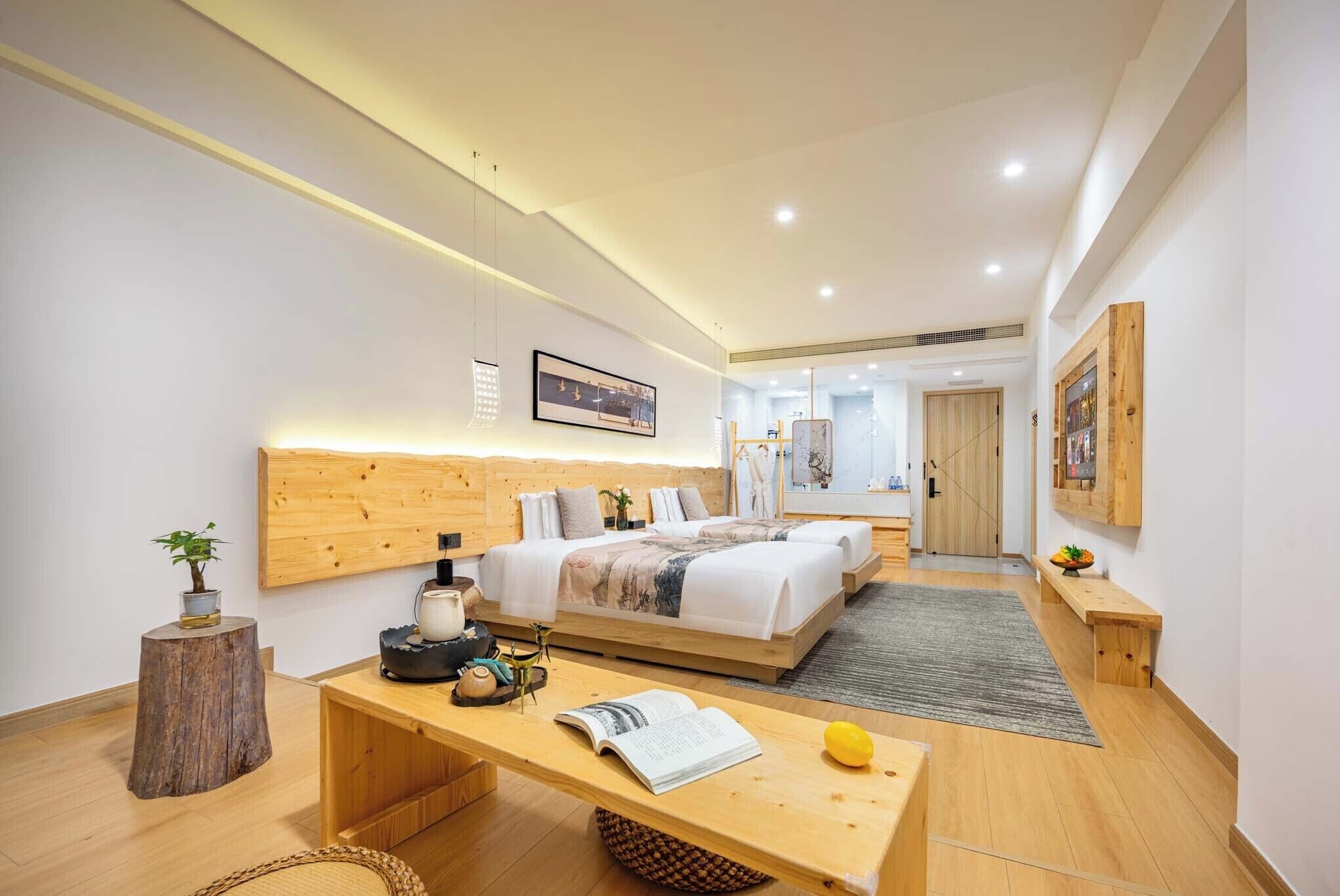 A modern bedroom with a wooden headboard, a large bed, bedside tables, a desk, and a small plant.