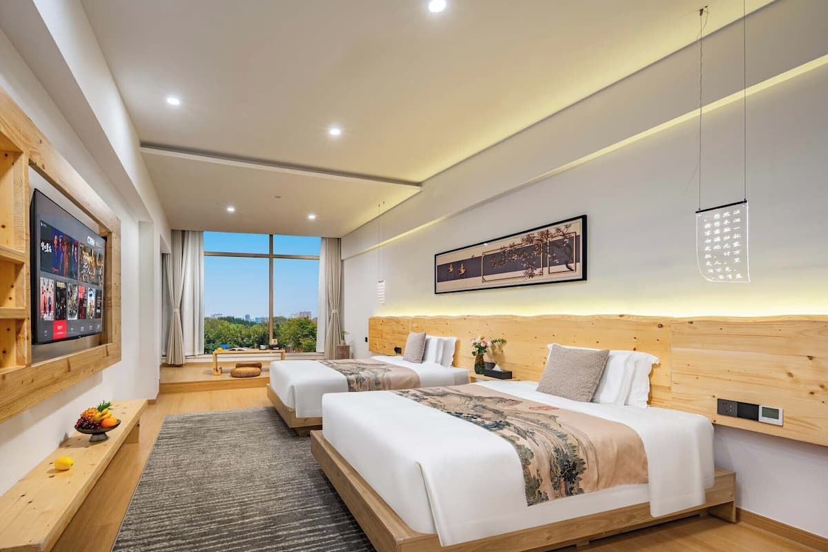 Una habitación de hotel moderna con dos camas, televisión, un ventanal grande y cabecero de madera.