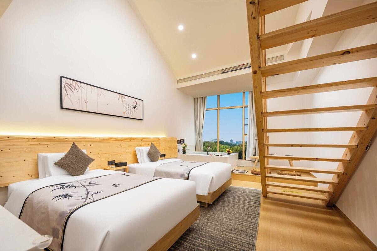 Habitación de hotel con dos camas, cabecero de madera, ventana grande y tragaluz.