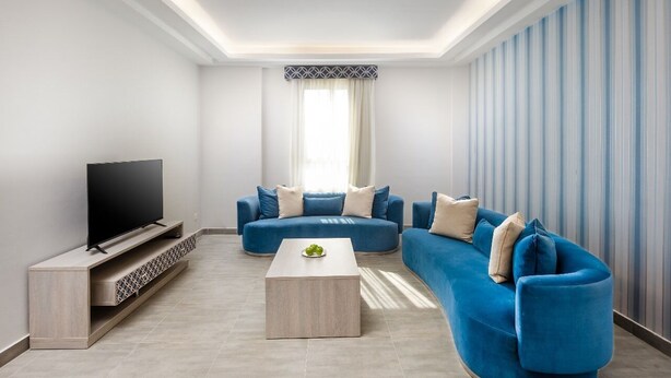 A modern living room with a flat-screen TV, blue sofas, a coffee table, and a patterned curtain. - Balensia Hotel (Madinah)