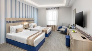 A hotel room with two beds, a desk, a chair, a TV, and a window with curtains. - Balensia Hotel (Madinah)