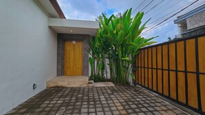Un edificio residenziale con una porta in legno, un muro in cemento, un patio piastrellato e un cancello in metallo.