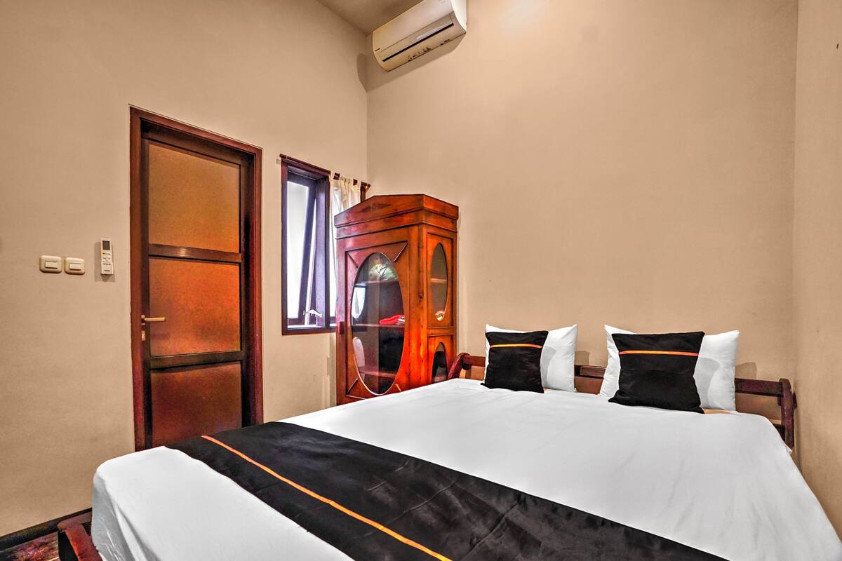 A hotel room with a bed, a wooden wardrobe, a door, and an air conditioning unit.