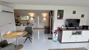 A modern living room with a TV, a dining area with a table and chairs, a kitchen area with a window, and a hallway leading to another room. - Extertal garden chalet with heated outdoor whirlpool Dogs free of charge (Extertal)