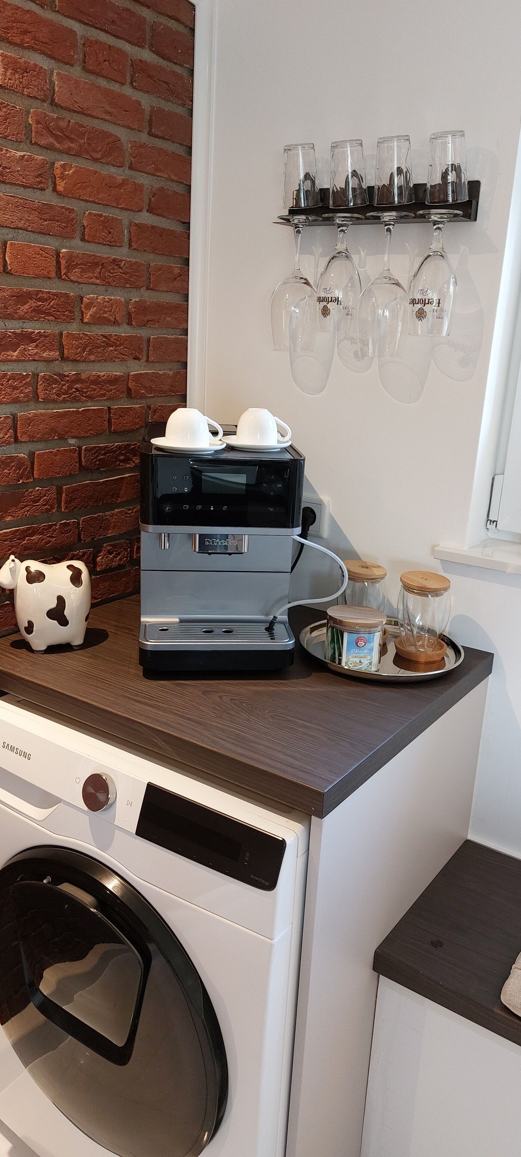 Eine Küche mit Mikrowelle, Waschmaschine und einem Regal mit Weingläsern.