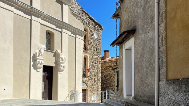 Una calle con un edificio de fachada de piedra y puerta blanca.