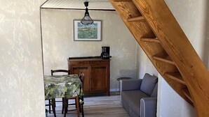 Un comedor con una mesa y sillas, una escalera de madera, un sofá y una cafetera.
