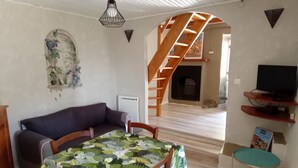 Una sala de estar con un sofá, una mesa con mantel de hojas, una escalera de madera, una chimenea y un televisor en un estante.