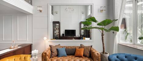 A living room with a brown sofa, a yellow armchair, a blue armchair, a large potted plant, and a flat-screen TV.
