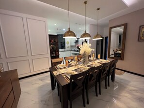 A dining area with a marble floor, wooden chairs, a central table with a vase of flowers, and pendant lighting. - Luxury ocean-view apartment in Colombo 03 (Colombo)