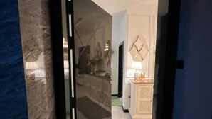 A modern interior with a glass door leading to a room with a white cabinet and a lamp.