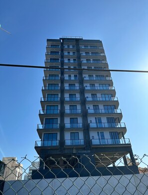 A multi-story building with balconies, a clear sky, and a chain-link fence in the foreground. - Luxury ocean-view apartment in Colombo 03 (Colombo)