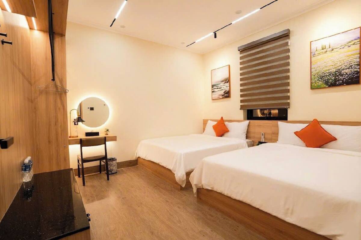 Une chambre d’hôtel avec deux lits, un bureau avec une chaise, un miroir et une fenêtre avec des stores.