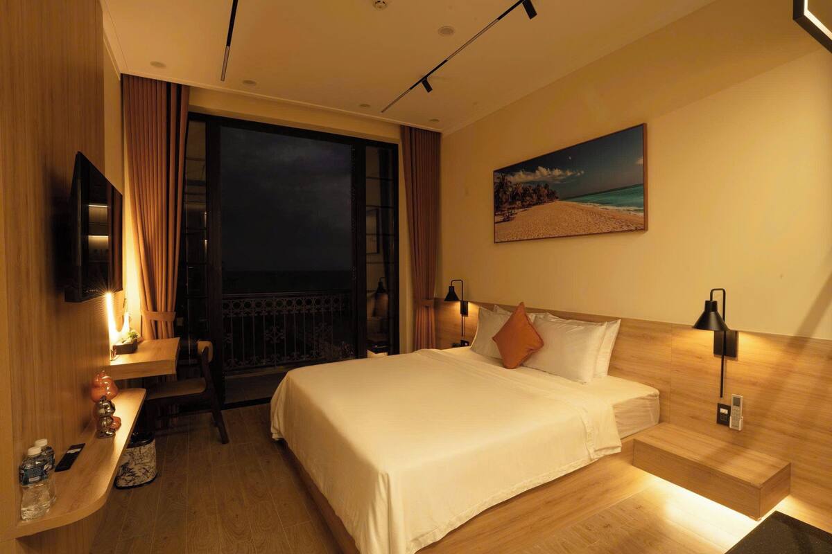 Une chambre d’hôtel équipée d’un lit, d’un bureau, d’une chaise, d’une télévision et d’un tableau représentant une scène de plage.